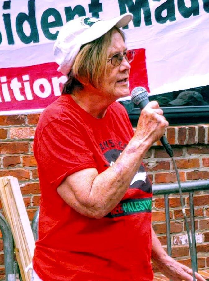 Photo of Ann Wright, an older white woman, speaking into a microphone. 