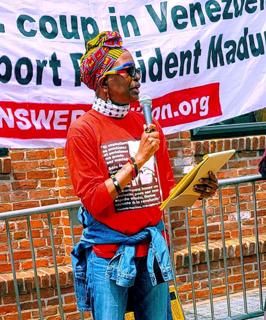 Photo of Asantewaa Nkrumah-Turi, a Black woman, speaking into a microphone in front of a banner. 