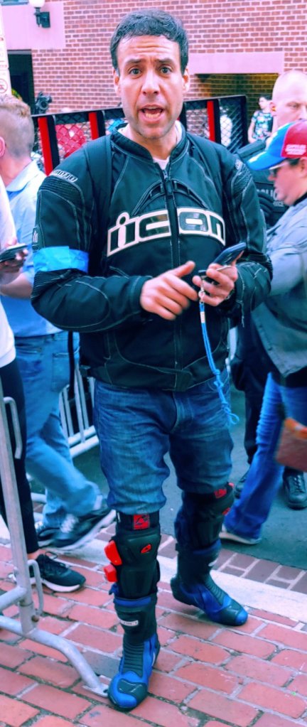 Photograph of a man wearing a motorcycle jacket and unusual boots with armored pads. 