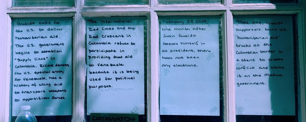 Photograph of windows, with a hand-written sign taped into each pane. 