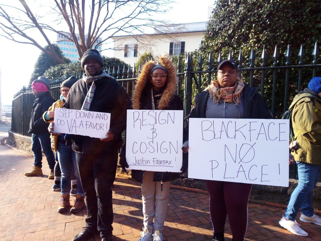 Photo of six demonstrators holding signs in front of a fence outside of the governor's mansion. The signs read: "Step down and do VA a favor!"; "Resign and co-sign Justin Fairfax!"; "Blackface No Place!"