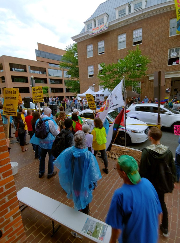 Photograph of a street: on one side, a crowd of anti-coup demonstrators, and on the other, clustered against the tall brick building of the Venezuelan embassy, the pro-coup demonstrators. 