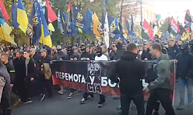 A very large crowd, primarily of young men, marching behind a black and red C14 banner.