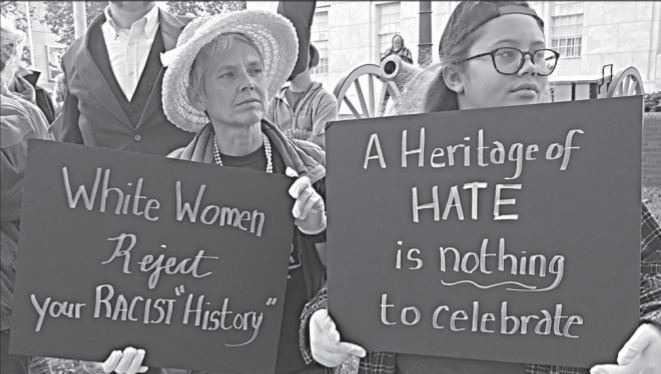 Two women holding signs that read "White women reject your racist 'history'" and "A heritage of hate is nothing to celebrate". 