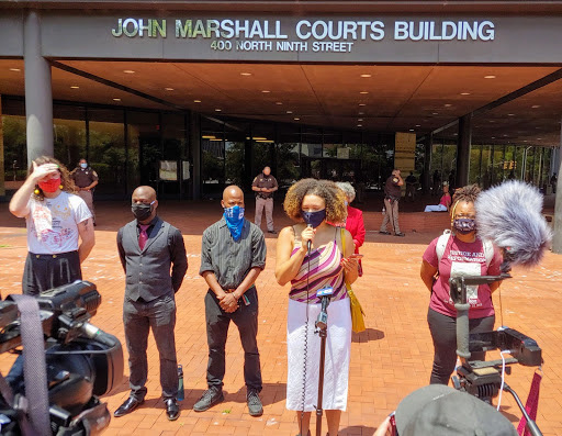 Photograph of Michaela Hatton and five others at a press conference in front of the John Marshall Court building in Richmond. Hatton is speaking. 