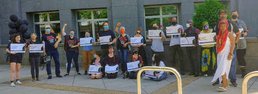 Photograph of 19 people with signs, roses, and black balloons gathered in front of a federal courthouse in Richmond. 