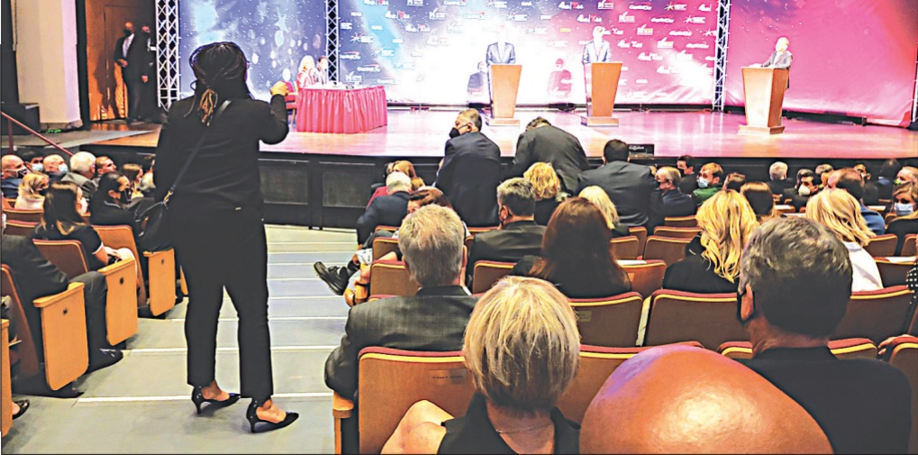A photograph of Princess Blanding, standing from the audience to confront the gubernatorial candidates and debate moderator on stage. The photo is taken from behind Blanding, with Youngkin, McAuliffe, and Todd visible on stage. 