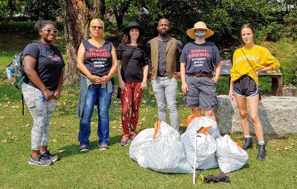 Six people, three Black and three white, posing behind five bags of trash. 