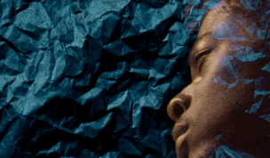 An artistic photograph depicting a Black face in profile on a backdrop of black crepe, with the background partially superimposed overtop. 